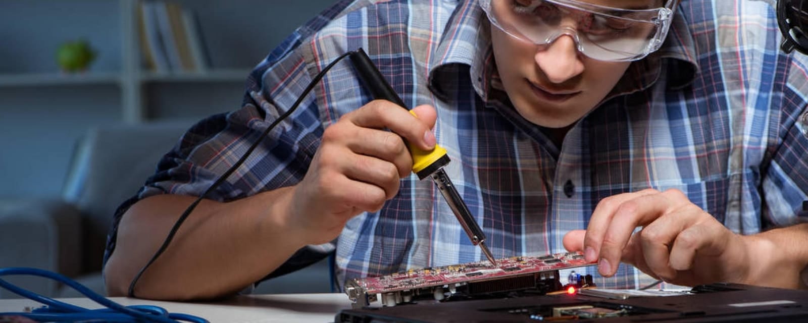 Homme avec lunettes de protection soudant une carte électronique avec un fer à souder.